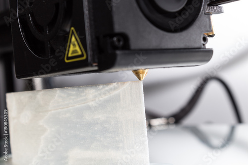 3D Printer Extruder Operation - Closeup view of a 3D printer's extruder in operation laying down white PVA plastic. photo