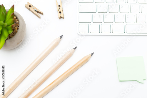 White keyboard with pencils and succulent on white background. Flat lay photo