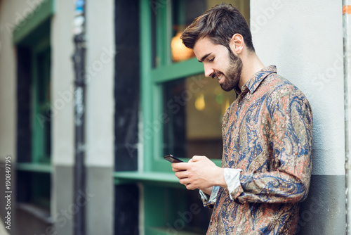 Young man wearing casual clothes looking at his smartphone in the street.