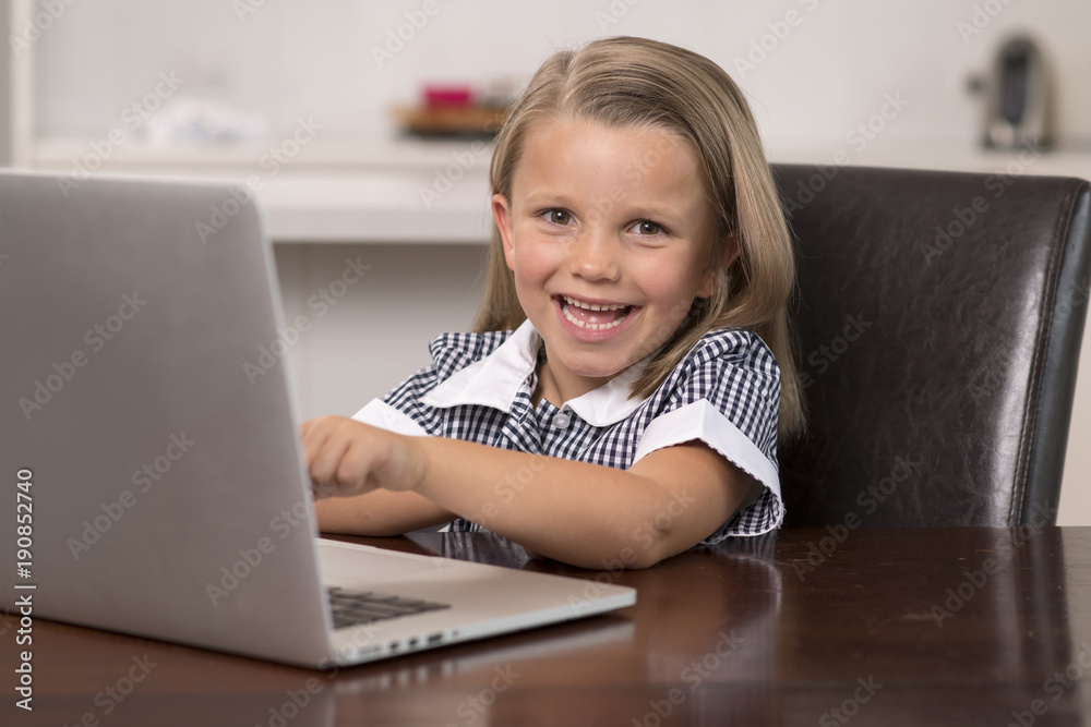 young beautiful and sweet little girl 6 to 8 years old with blond hair and blue eyes sitting at home kitchen enjoying with laptop computer smiling happy young beautiful and sweet little girl 6 to 8 years old with blond hair and blue eyes sitting at home kitchen enjoying with laptop computer smiling happy