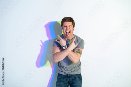 Portrait of happy man with colorful shadow putting out tongue while gesturing hands. Rock and roll concept