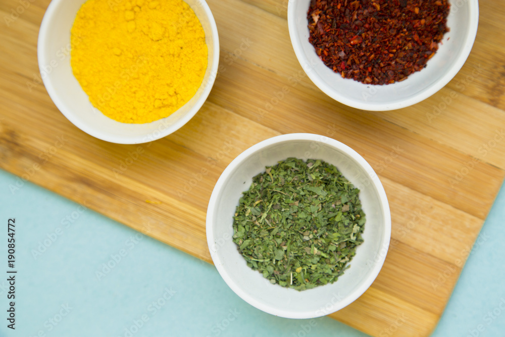 Plastic cups with dry spices and fresh herbs on a wooden cutting board with blue background, top view, close up Plastic cups with dry spices and fresh herbs on a wooden cutting board with blue background, top view, close up