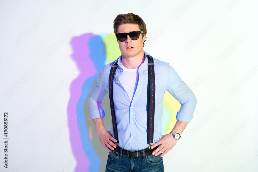 Portrait of assertive male in sunglasses with hands on hips. He has multicolored shadow. Assuredness concept Portrait of assertive male in sunglasses with hands on hips. He has multicolored shadow. Assuredness concept
