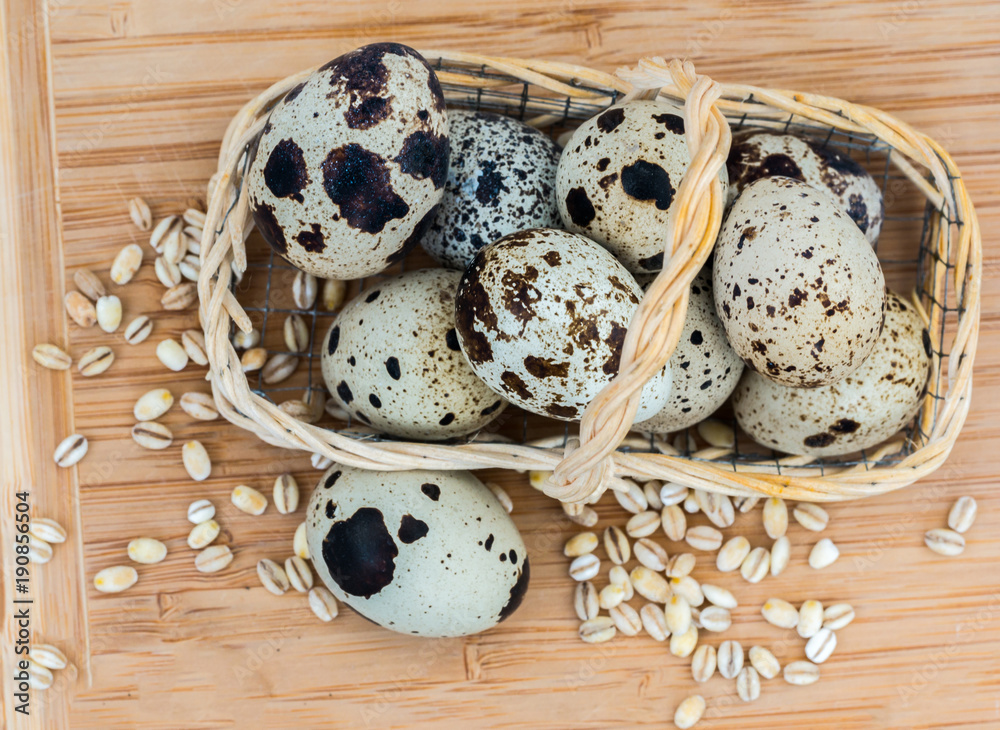Quail eggs in wicker basket and grains of barley on wooden table. View from above Quail eggs in wicker basket and grains of barley on wooden table. View from above