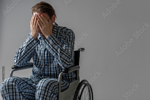 Decadent male person sitting in wheelchair and covering his face with hands. He is crying. Copy space in right side. Isolated on background