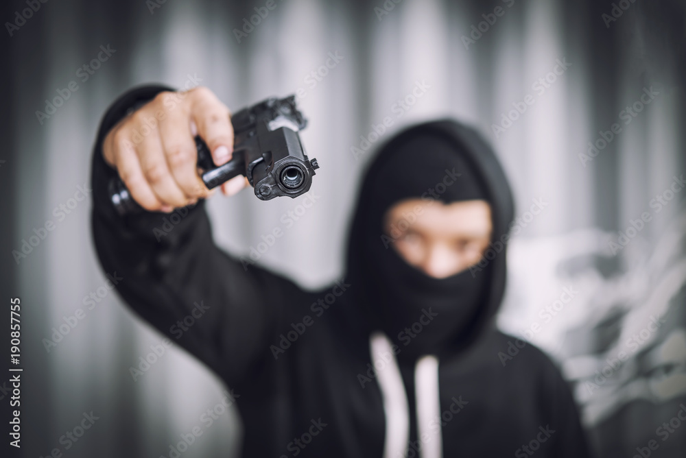 Masked robber with gun aiming into the camera with monochrome background. Dangerous gun man as bandit. Masked robber with gun aiming into the camera with monochrome background. Dangerous gun man as bandit.