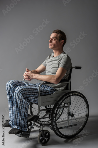 Disease concept. Side view of thoughtful invalid taking seat in special armchair