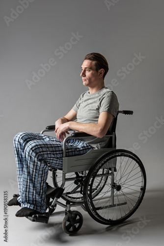 Ruined life concept. Side view of depressed male person disabled sitting in wheelchair photo