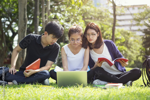 Education concept, group of students reading and doing homework and report with computer outdoor on grass in university or school. Prepare and intend to study with happiness.