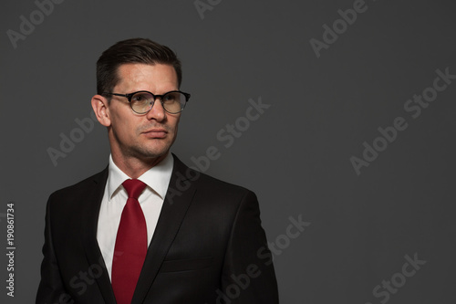 Portrait of positive businessman in formal attire and glasses looking to the side on gray background. Place for text.