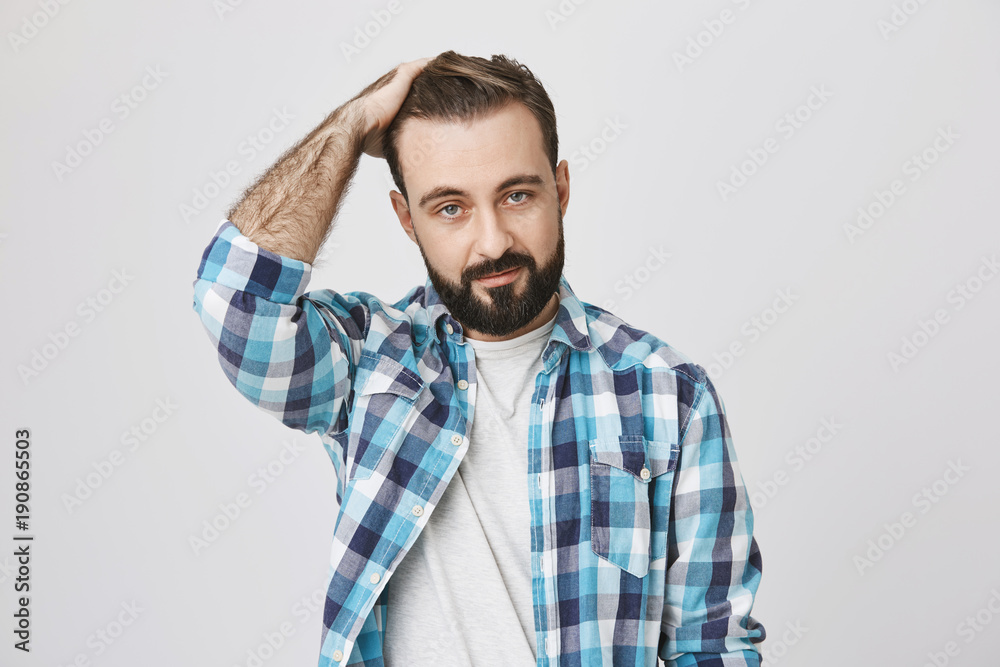 Studio shot of elegant bearded guy with moustache and trendy haircut, holding hair on head and expressing confidence while looking at camera, over gray background. Macho came to bar to meet somebody Studio shot of elegant bearded guy with moustache and trendy haircut, holding hair on head and expressing confidence while looking at camera, over gray background. Macho came to bar to meet somebody