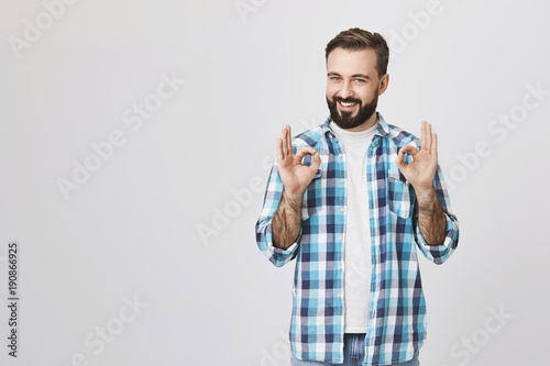 Portrait of happy handsome bearded male saying everything is okay and fine with gesture, standing over gray background. Hey, I got it, everything will be done perfectly photo