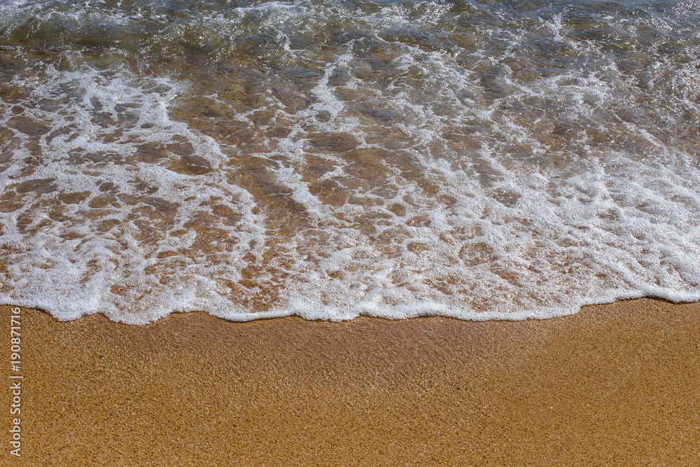 The concept of beach holidays and tourism. Background close-up of a sea wave with foam on yellow sand. The Mediterranean Sea in Spain The concept of beach holidays and tourism. Background close-up of a sea wave with foam on yellow sand. The Mediterranean Sea in Spain