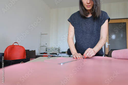 seamstress got high-quality material for bags from friend living abroad. Smiling girl with kare haircut and red nails unwrapping roll of leather on table in workshop at home. Concept of expen photo