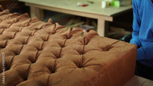 Handyman is upholstering back of the couch with brown velour. He is folding parts of velour and stapling it. photo