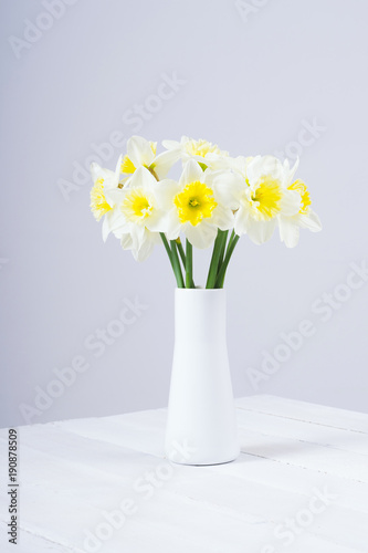 white daffodils at china vase on bright wood table