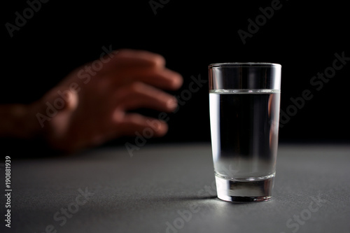 hand reaches for a glass of vodka or alcohol drink, alcoholism and alcohol abuse concept, defocused,.selective focus, close up, gray table, dark background