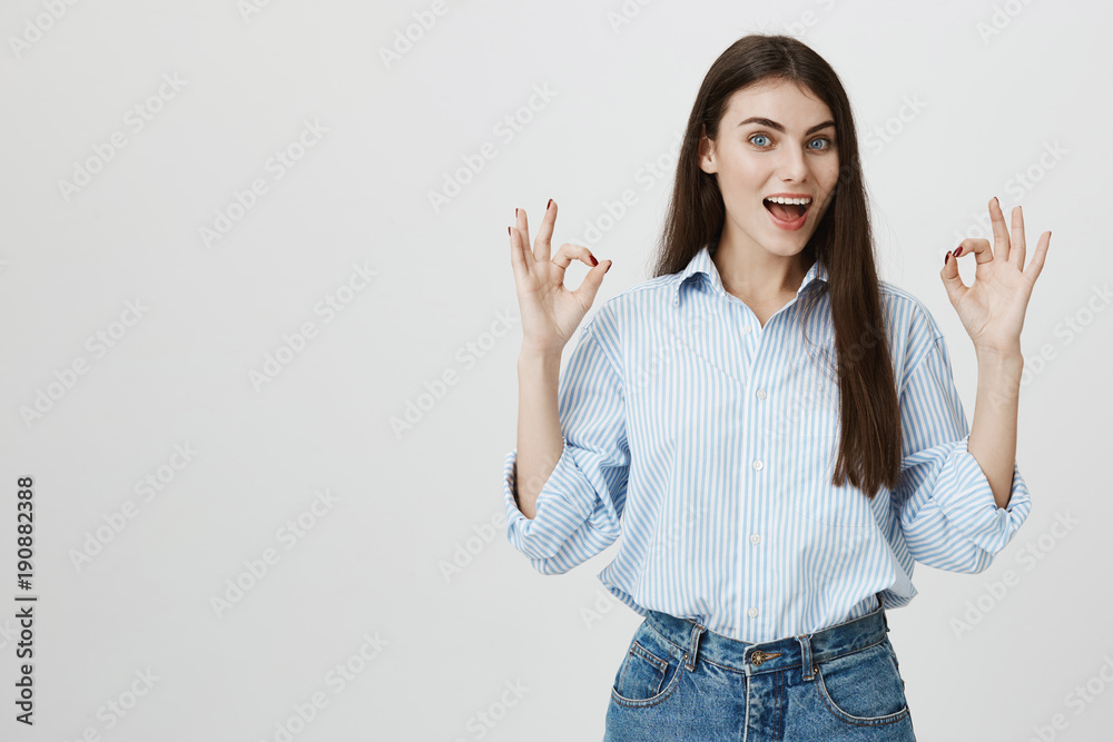 Excited and emotive caucasian female student, showing okay or great sign with both raised hands and expressing positive reply while standing over gray background. Girl rent her first apartment Excited and emotive caucasian female student, showing okay or great sign with both raised hands and expressing positive reply while standing over gray background. Girl rent her first apartment