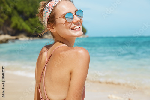 Nature, tourism and summer holidays concept. Back view of slim attractive female traveler spends free time in beautiful and peaceful remote place, poses against blue seascape with rocky cliff