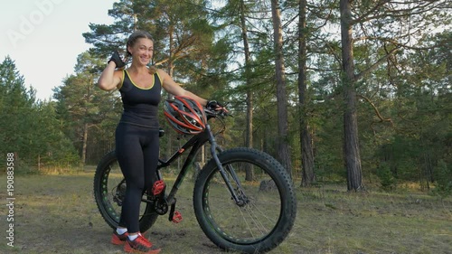 Fat bike also called fatbike or fat-tire bike in summer riding in the forest. Beautiful girl and her bicycle in the forest. She is posing and pampering near the bicycle.
