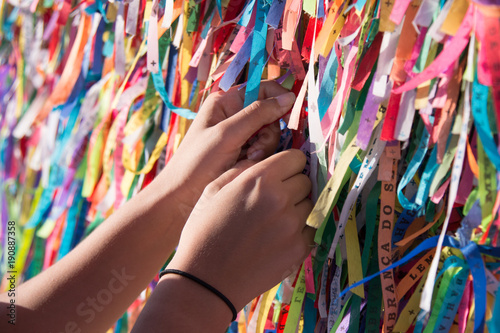 Female hands tying colored ribbons on grid in front of Bonfim church in Salvador, Bahia, Brazil
