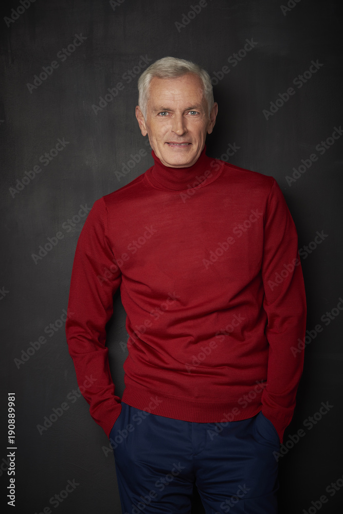 Casual senior man portrait. Handsome elderly man wearing red turtle neck sweater and looking at camera while standing against at dark background.