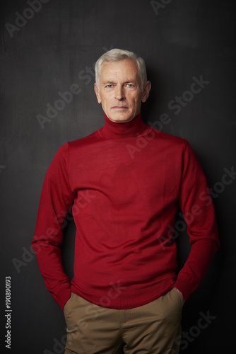 Casual senior man portrait. Handsome elderly man wearing red turtle neck sweater and looking at camera while standing against at dark background. © gzorgz