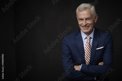 Smiling business man portrait. Executive senior lawyer businessman wearing suit and looking at camera while standing at isolated black background with copy space. 