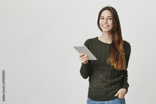Waist-up portrait of smiling positive caucasian female model in casual clothes expressing positive emotions while reading article from tablet computer. Modern technologies concept