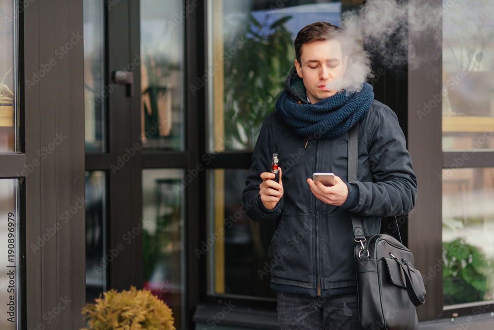 Vaping. Portrait of man vaping a vaporizer outdoors. Safe smoking. Young vaper. Close-up. Vaping. Portrait of man vaping a vaporizer outdoors. Safe smoking. Young vaper. Close-up.