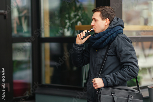 Young man vaping an electronic cigarette outdoor. Casual man smoke vaporizer. Vaping