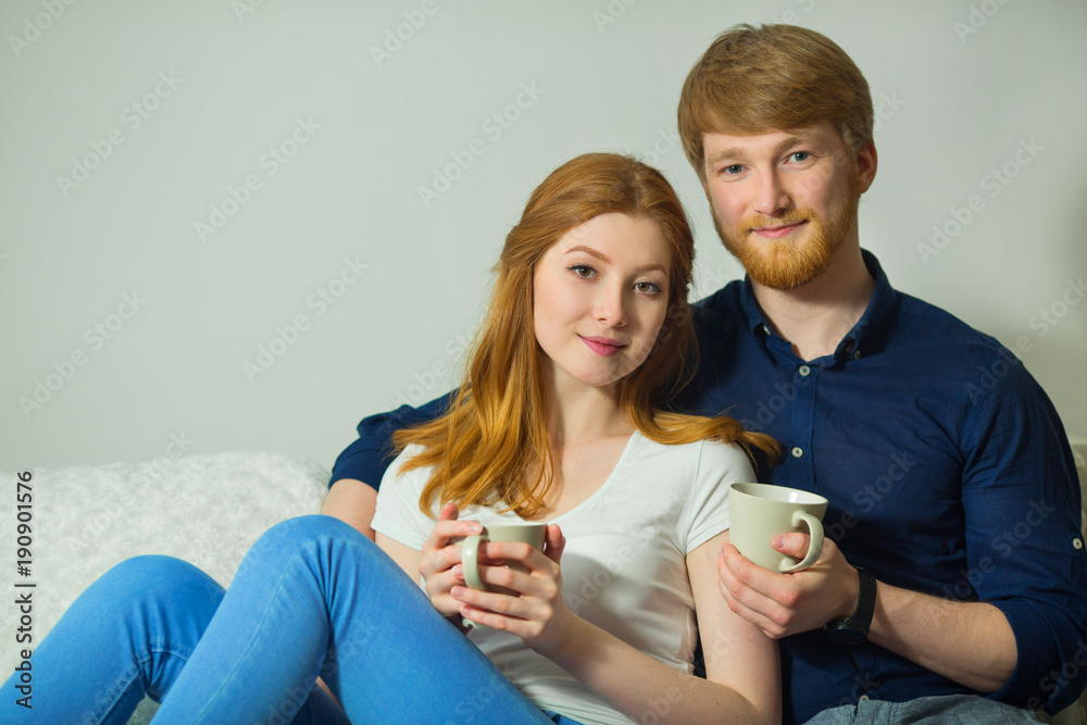 beautiful young couple guy with a girl with red hair sitting on the couch and drinking tea beautiful young couple guy with a girl with red hair sitting on the couch and drinking tea