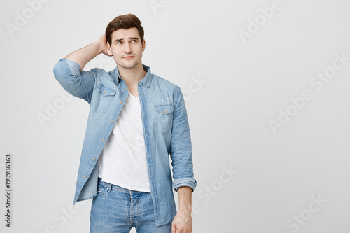 Horizontal portrait of handsome male adult with stubble, keeps hand on back of his head, listens to someone`s official speech, analyzes information or makes decision. People and lifestyle