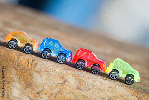 Fototapeta Naklejka Na Ścianę i Meble -  line of transparent coloured toy cars on stone heading downhill with sharp gradient