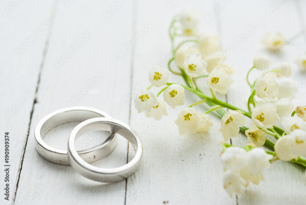 Φωτογραφία Lily of the valley with wedding rings on white wooden