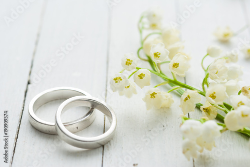 Lily of the valley with wedding rings on white wooden