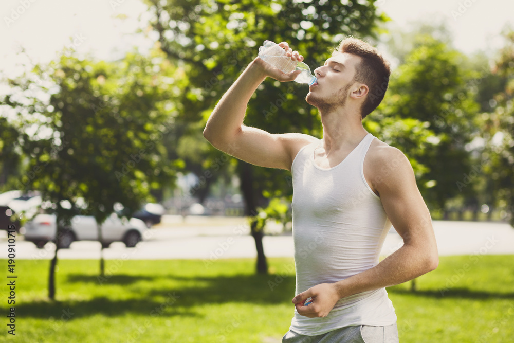 Fitness man drinking water in park otdoors Fitness man drinking water in park otdoors