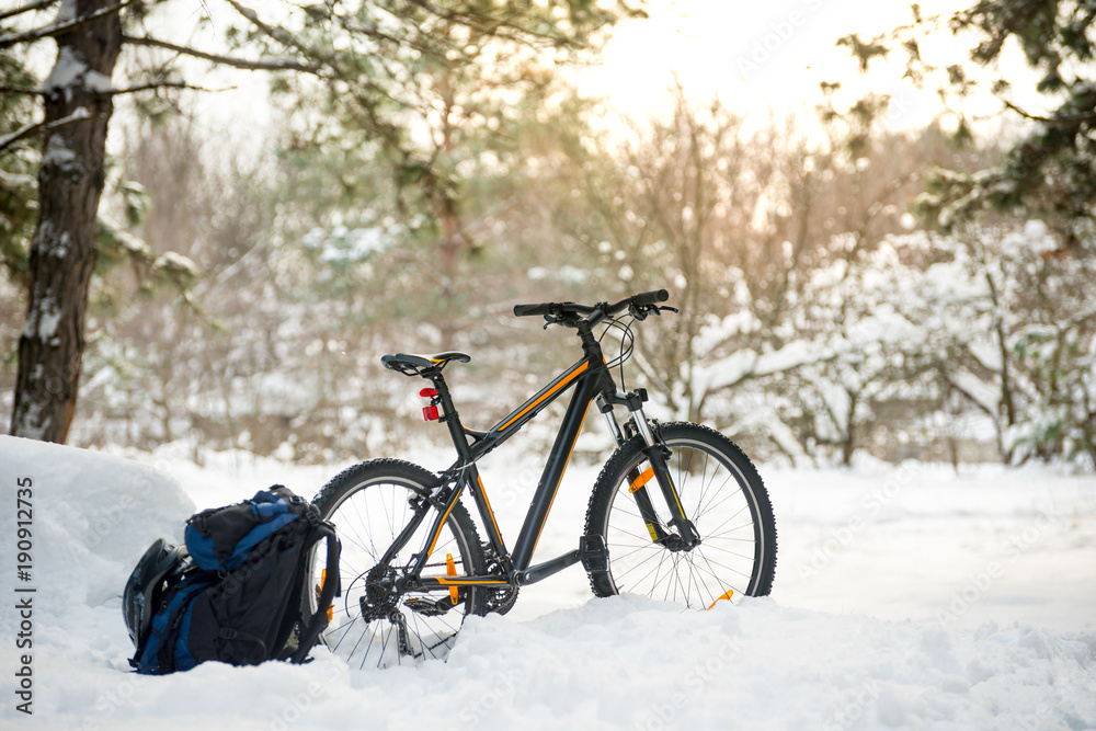 Mountain Bike with Backpack and Helmet in Beautiful Winter Forest Lit by the Sun. Adventure and Travel Concept. Mountain Bike with Backpack and Helmet in Beautiful Winter Forest Lit by the Sun. Adventure and Travel Concept.
