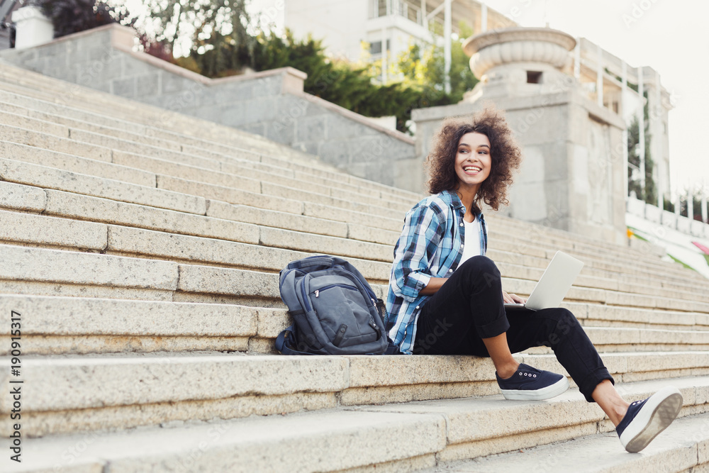 Smiling student sitting on stairs using laptop Smiling student sitting on stairs using laptop