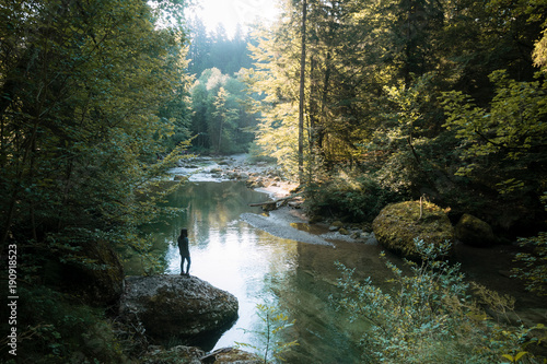 Calm forest with river and female hiker standing on a stone overlooking the water in Germany photo