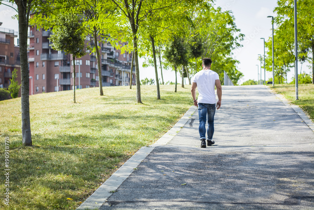 Back of muscular man in city park in a nice summer day walking. Full length shot Back of muscular man in city park in a nice summer day walking. Full length shot