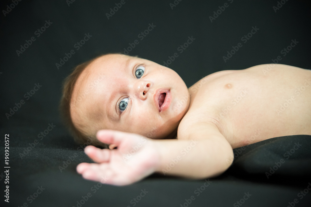 Blue eyed naked baby lying on black fabric Blue eyed naked baby lying on black fabric
