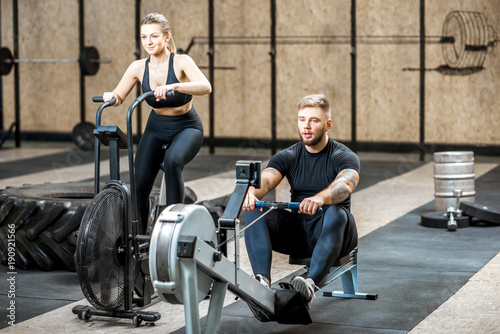 Young couple training on the exercise air bicycle and rowing machine in the gym photo