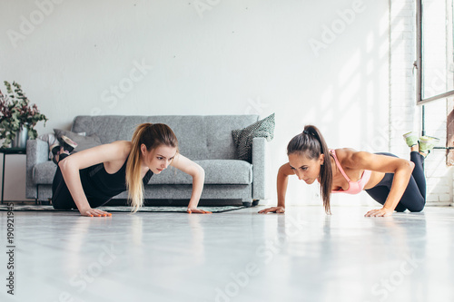 Two fitness women warming up doing push-ups exercise working out at home