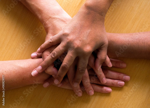 looking down on four hands placed ontop of each other, the top hand and third hand are Asian and the second and forth are caucasian