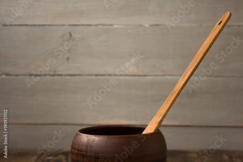 clay pot with a wooden spoon on a wooden background