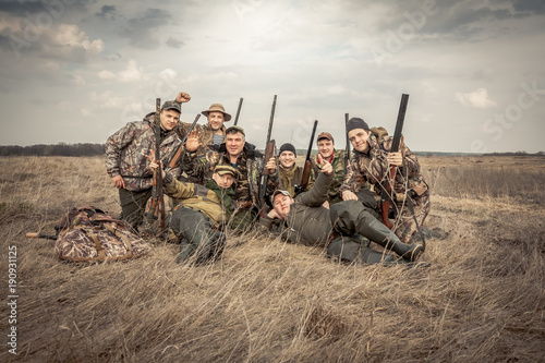 Obraz na plátne Men hunters group team portrait in rural field posing together against overcast sky during hunting season