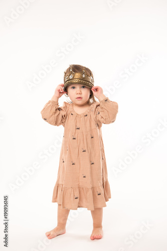 Cute little girl in beige dress with gold crown isolated on white background. Portrait of happy little girl.