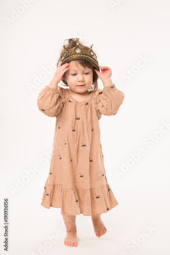 Cute little girl in beige dress with gold crown isolated on white background. Portrait of happy little girl.