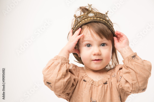 Cute little girl in beige dress with gold crown isolated on white background. Portrait of happy little girl.